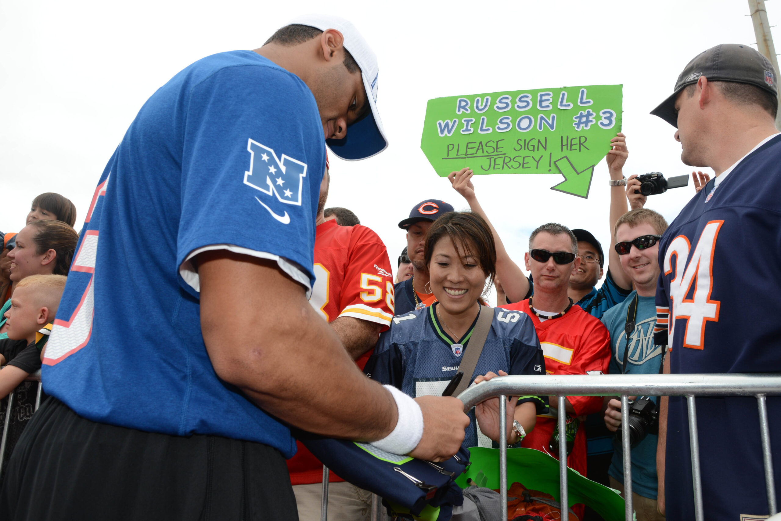 NFC quarterback Russell Wilson of the Seattle Seahawks (3, left) autographs a jersey for Erin Furukawa (center), from Hawaii, during practice for the 2013 Pro Bowl at Joint Base Pearl Harbor-Hickam.