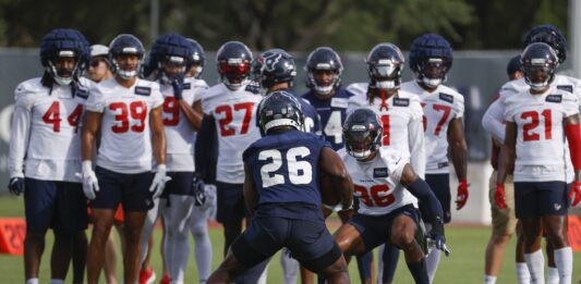 Houston Texans players performing a drill at minicamp while other players look on.