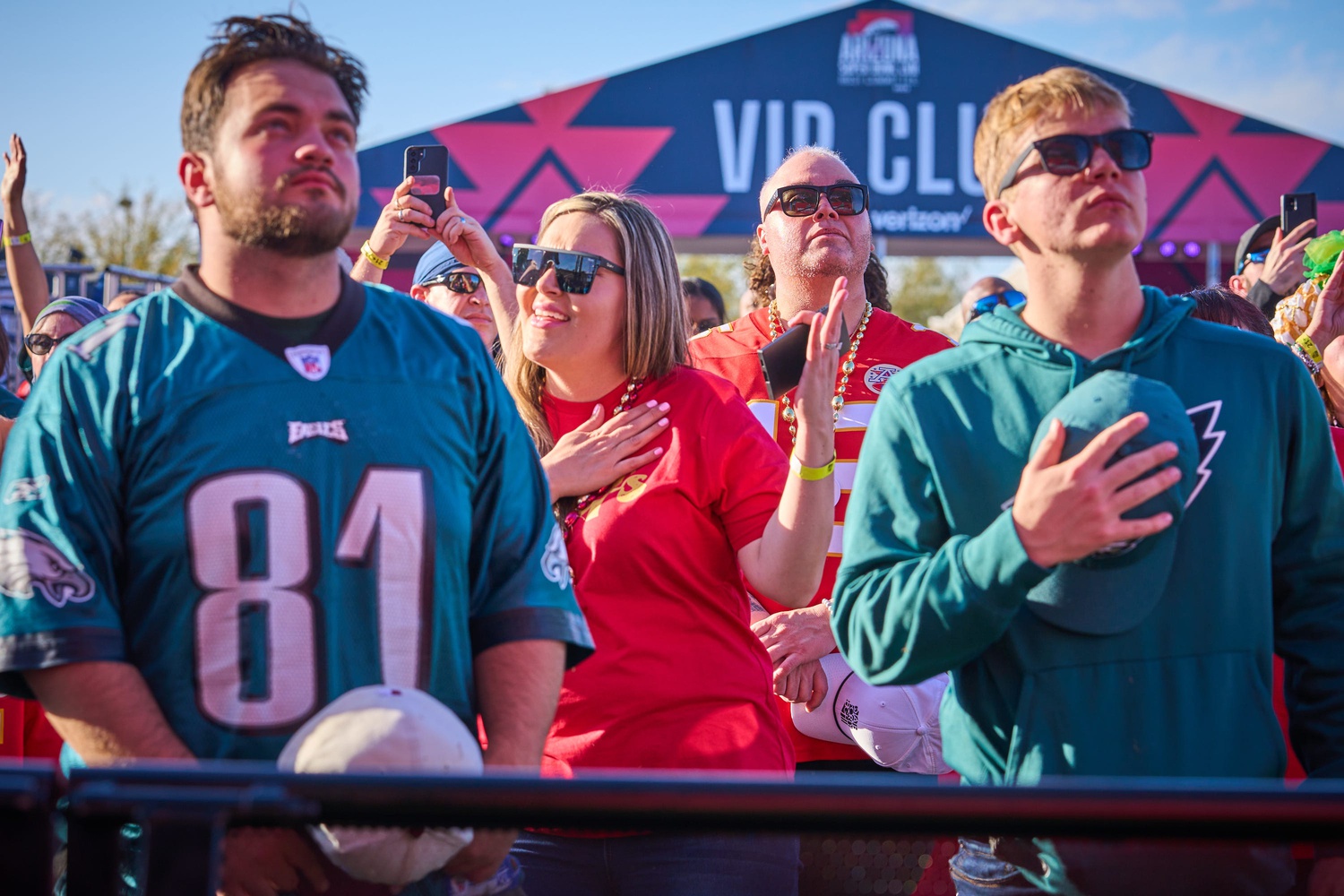 Fans stand with their hands over their hearts during America the Beautiful at the NFL's official Super Bowl LVII watch party.